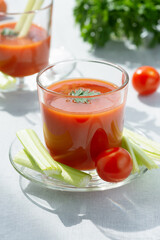 Two glasses with fresh tomato juice, celery, parsley and ripe tomatoes 