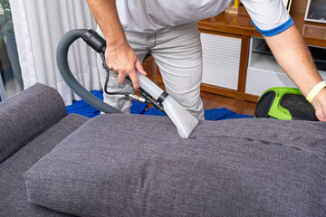 Man using a special vacuum to clean gray sofa cushions_side view.