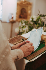hands of a Christian priest signing a baptismal certificate during a baptism ceremony in a...