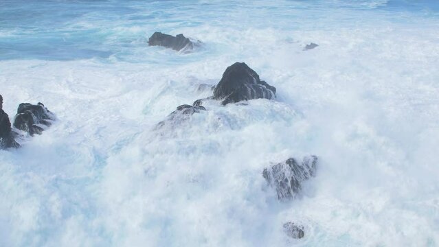 A big waves of the Atlantic Ocean breaks on a rocky coast on a sunny day during a storm in Puerto de la Cruz in the Canaries (Tenerife, Spain), medium handheld shot