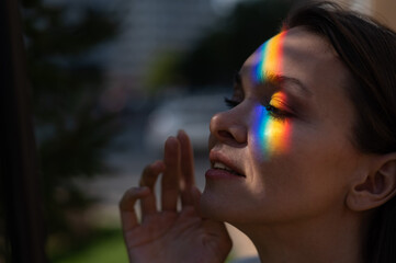 Portrait of caucasian woman with rainbow beam on her face outdoors.