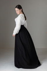 Naklejka premium A young Victorian or Edwardian woman wearing a white linen Garibaldi blouse and a black skirt against a studio backdrop