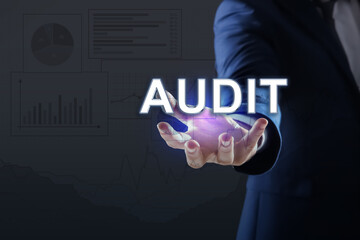 Audit concept. Businessman holding digital word in hand on dark background, closeup. Graphs and...
