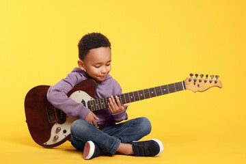 African-American boy with electric guitar on yellow background