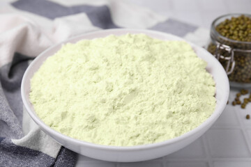 Mung bean flour in bowl and seeds on white tiled table, closeup
