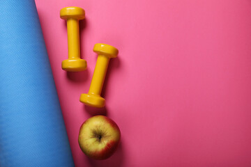 Fitness mat, dumbbells and apple on pink background, flat lay with space for text. Morning exercise