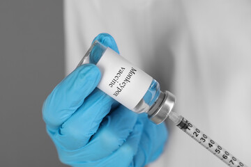 Nurse filling syringe with monkeypox vaccine from glass vial on grey background, closeup