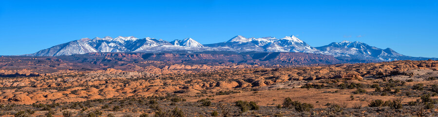 Fototapeta na wymiar La Sal Mountains - Panoramic view of snow-capped La Sal Mountains, towering above a vast field of orange petrified dunes and red sandstone mesa, on a sunny Winter day. Arches National Park, Utah, USA.
