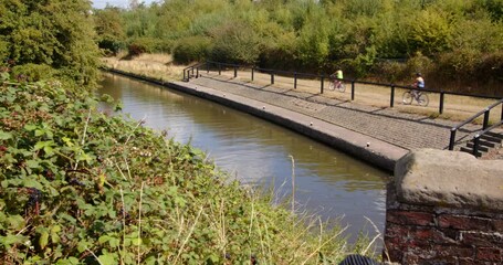 Wide shot from Aston Lock looking down on to Trent and Mersey Canal with 3 famley Cyclist cycling through the shot.