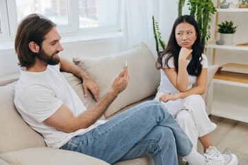 A man looks at the phone screen during an argument with his girlfriend. The angry and hurt woman...