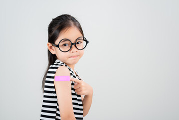 Asian little girl wear glasses showing her arm with bandage after virus vaccine happy Kid and child...