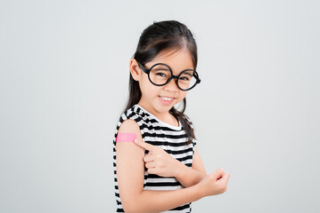 Asian little girl wear glasses showing her arm with bandage after virus vaccine happy Kid and child vaccination campaign. Protect your kid with vaccine concept