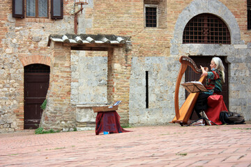 magical woman plays the harp in an ancient square in the romantic tuscan town of san gimignano