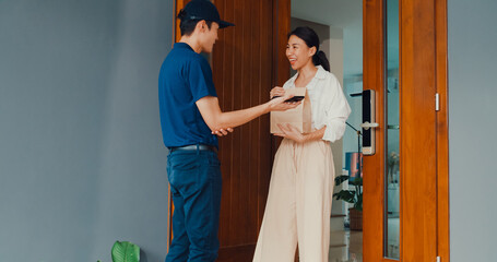 Young Asian delivery man in blue navy uniform knock door home delivery grocery online shopping to...