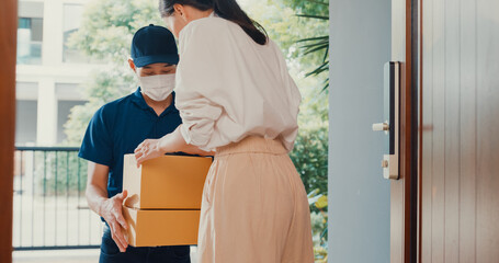 Young Asian delivery man wear mask in blue navy uniform carry case box knock door home online shopping cardboard box to woman in front of door lady scan QR code payment on smartphone at house concept.