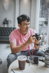 Asian man with retro vintage film camera with photo from film in cafe, Thailand.