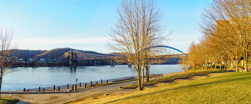 Panoramic View Of The Ohio River With The Landmark 1856 Wheeling Suspension Bridge And The 1955 Fort Henry Bridge, Seen From Heritage Port Waterfront Park, Wheeling, West Virginia.  January 2022.