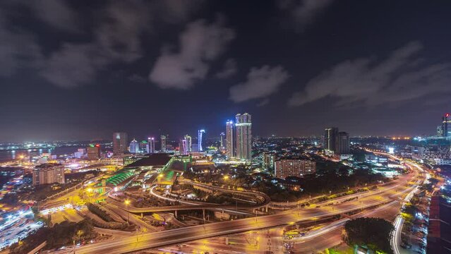 Aerial time lapse of Johor Bahru city with tall buildings from afar in clear sky at night and busy traffic on elevated highway. Tilt down motion timelapse. Prores 4KUHD