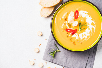Bowl of spicy pumpkin cream soup garnished with seasonings and red chili pepper. Thick butternut squash bisque in green bowl over white table. View overhead. Minimal style. Selective focus