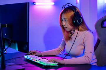 Happy Gamer endeavor plays online video games tournament with computer neon lights, young woman wearing gaming headphones intend to do playing live stream games online at home