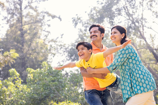 Cheerful parents assisting son in flying at park.