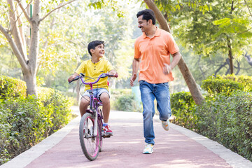 Boy learning bicycle with assistance of father at park