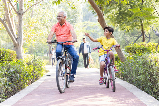 Happy grandfather and grandson riding bicycle at park.