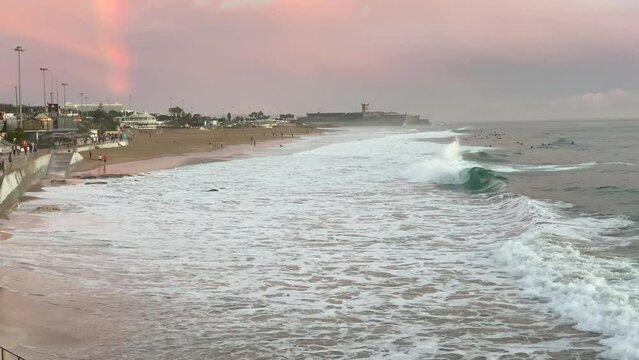 Incredible beautiful sunset sky reflections of Atlantic ocean waves at Carcavelos beach near Lisbon, amazing orange teal and blue tones, some people walking.