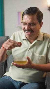 Vertical shot of happy middle aged man eating gulab jamun sweet or desserts at home - concept of Medical, diabetes and healthcare