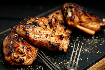 Close-up appetizing BBQ chicken thighs on a black cutting board. Soft focus.