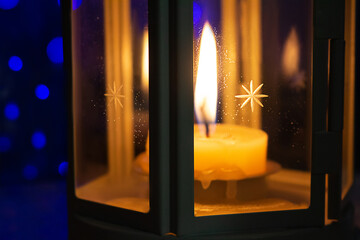 Lantern with burning candle in dark. Behind blue bokeh. Holiday atmosphere, Christmas, New Year. Selective focus