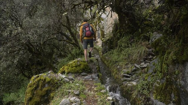 Male Backpacker Trekking On Rocky Hiking Trail With Stream Flowing In Huaraz, Peru. static