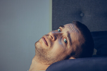 Dramatic lifestyle portrait of a handsome guy in his 30s and 40s, sitting sadly on the bed, feeling...