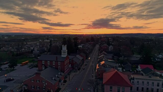 A Drone Approaching a View of a Small Town and a Steeple at Sunrise with Orange and Reds on a Spring Sunrise With Partial Cloudy Skies.
