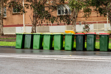 Australian garbage wheelie bins with yellow and red lids for recycling and household waste lined up on the street near residential building for council rubbish collection.