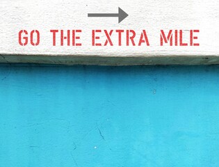 Old white blue wall with text inscription direction GO THE EXTRA MILE, concept of to do more than what people expect,.to give someone better experience than they expect