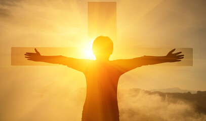 The boy stood with his arms outstretched, with a cross in front of him and sky light.