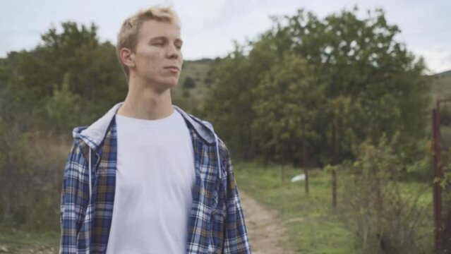 man in country clothes is walking on village. Tall guy going of road to horse paddock among nature. Autumn after rain middle day time. Around trees and fields