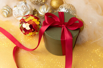 New Year and Christmas background. Christmas golden balls and green round gift with red ribbon on a yellow background with angel hair. Top view