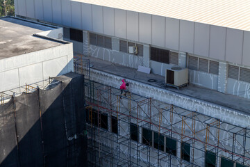 Workers are using tools to repair building walls to repaint by scaffolding at dangerous heights.