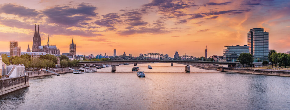Panoramic view of the city of Koln, the Rhine River, bridges and various barges and ships during majestic sunset.