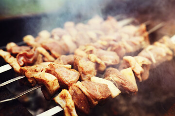 Selective focus. Cooking barbecue on the mangal in nature. Grilled tasty meet cooking on the party. Traditional Russian shashlik on a barbecue skewer on sunny forest.
