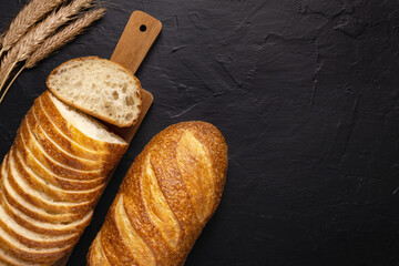 Fresh wheaten baton bread on dark background. Top view. Copy space