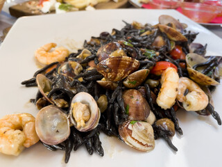 Black pasta with clams and shrimps. Italian seafood on white plate