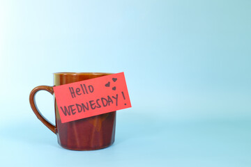 Welcome, hello and happy Wednesday concept. Selective focus of coffee cup with written message isolated in blue background.