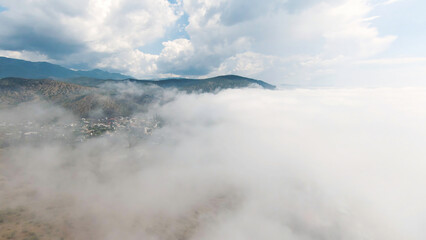 Top view of thick clouds with mountain peak on horizon. Schot. Flying in cloudy sky with dense clouds from top of mountain. Landscape of top of green mountain on horizon among white clouds