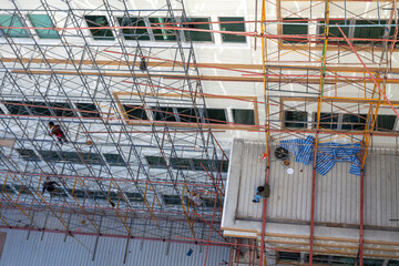 A construction worker sitting on the roof of a high-rise building repairing the exterior of the building