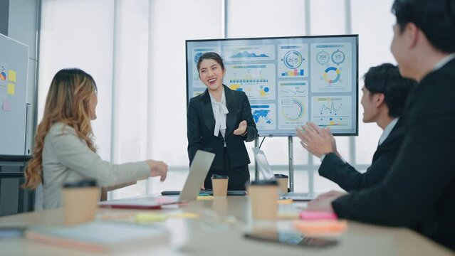 Professional asian businesswoman standing by the interactive board making presentation of projectand with successful teamwork applauding sitting in the meeting room