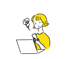 ノートパソコンの前で携帯電話を見る女性