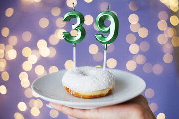woman holding a cake with the number 39 candles on festive blurred bokeh background